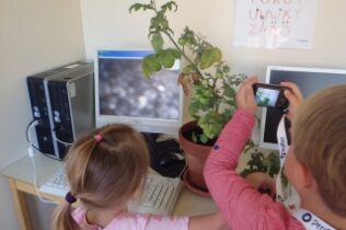 Barn fotograferar en tomatplanta på ett skrivbord framför en dator.