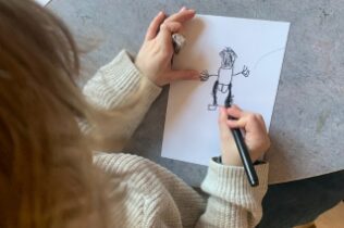 Barn ritar en mänsklig figur på papper, en del av ett språkutvecklande projekt i förskolan med koppling till Hasse Alfredson.