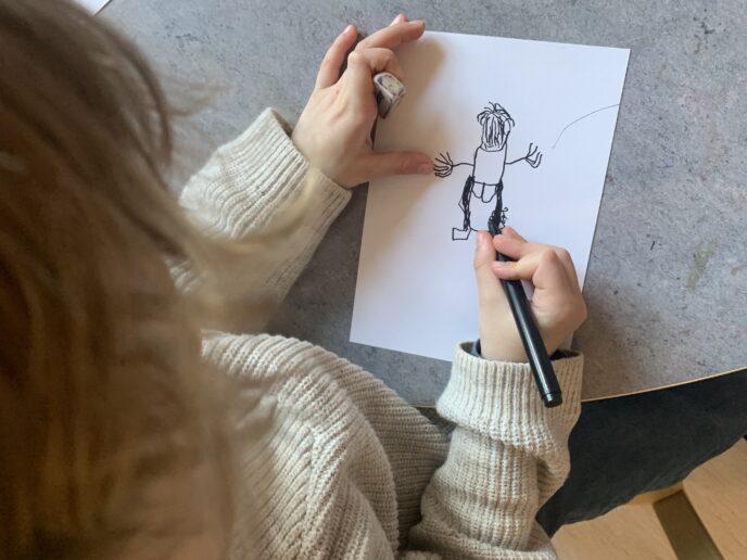 Barn ritar en mänsklig figur på papper, en del av ett språkutvecklande projekt i förskolan med koppling till Hasse Alfredson.